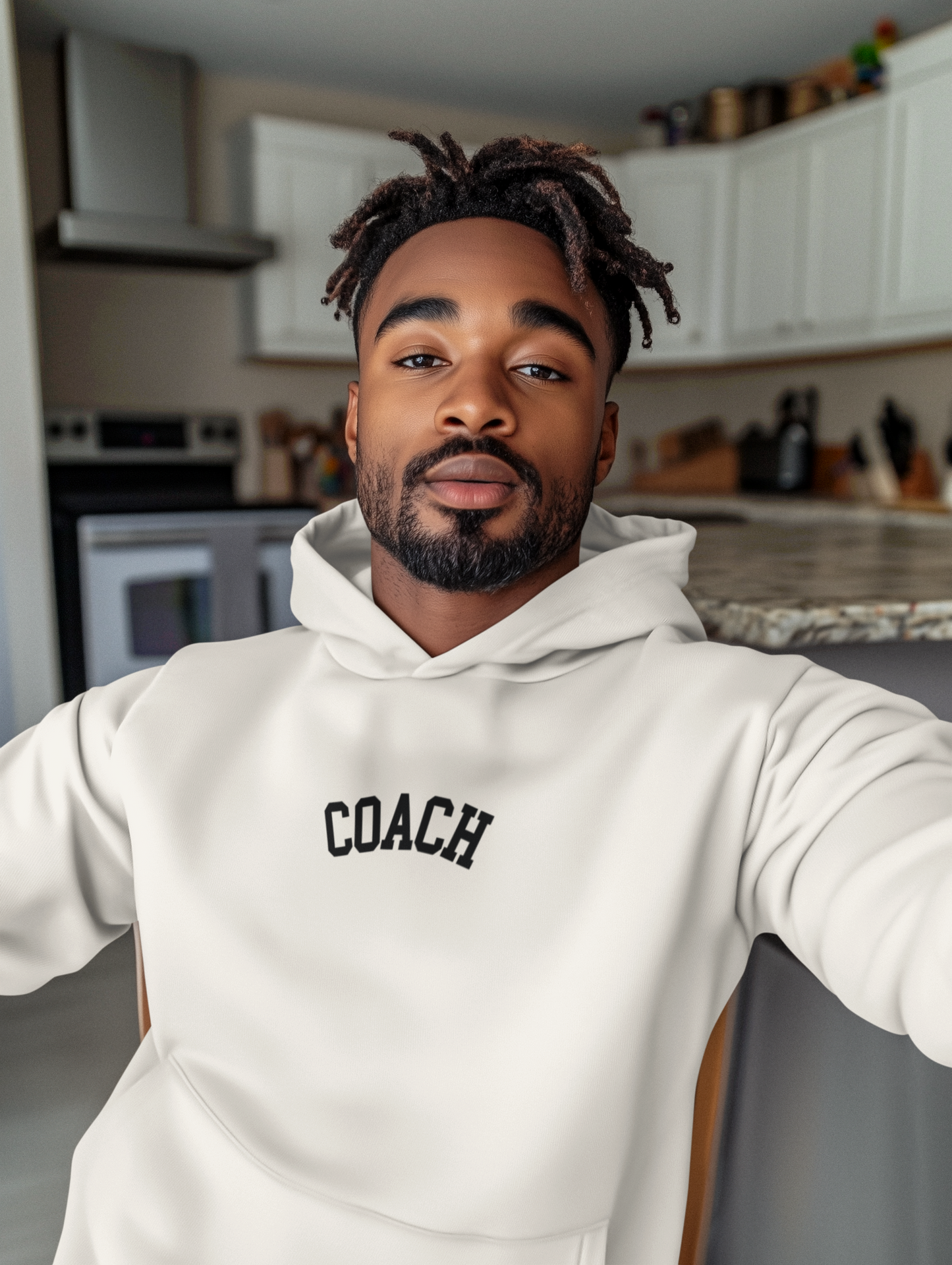 Man wearing a white hoodie with 'COACH' text in a kitchen setting