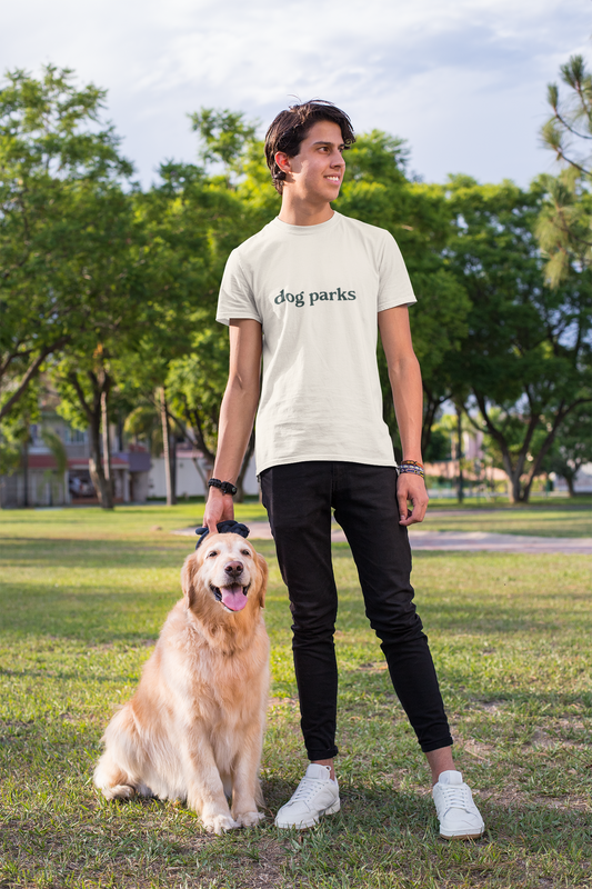 Person wearing a 'dog parks' t-shirt standing with a dog in a park.