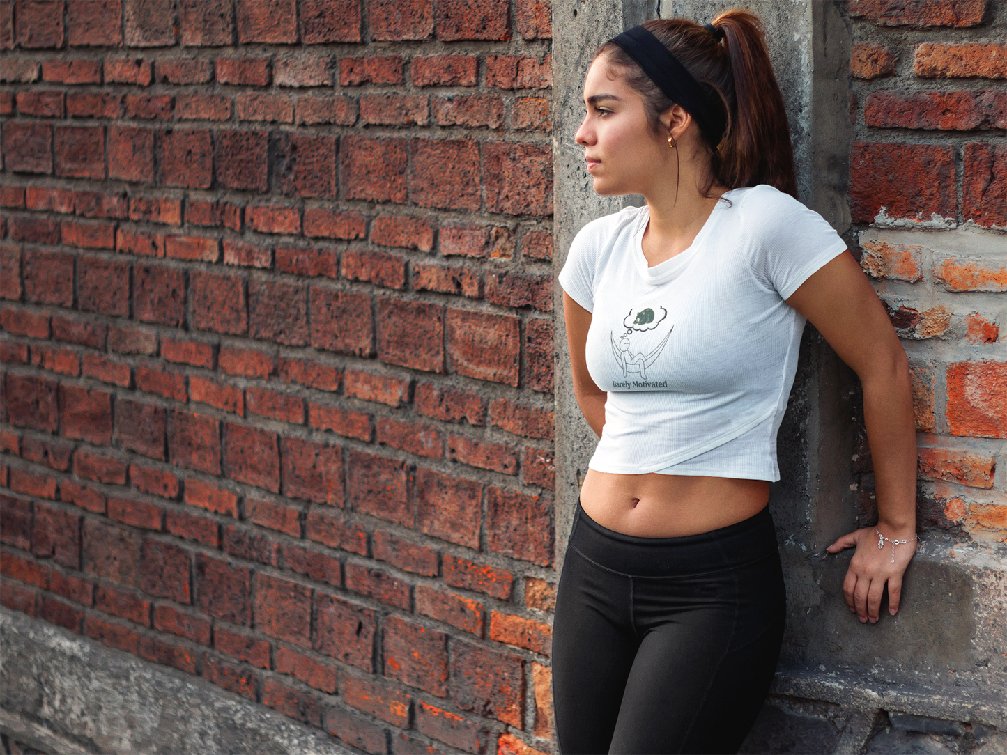 Woman leaning against a brick wall wearing a white t-shirt and black leggings.