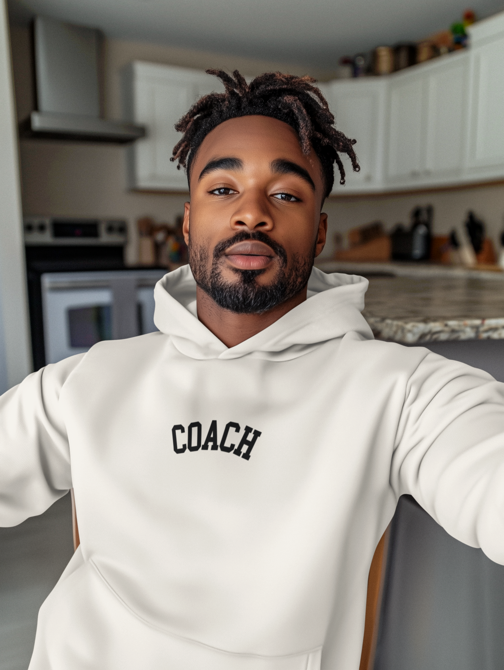 Man wearing a white hoodie with 'COACH' text in a kitchen setting