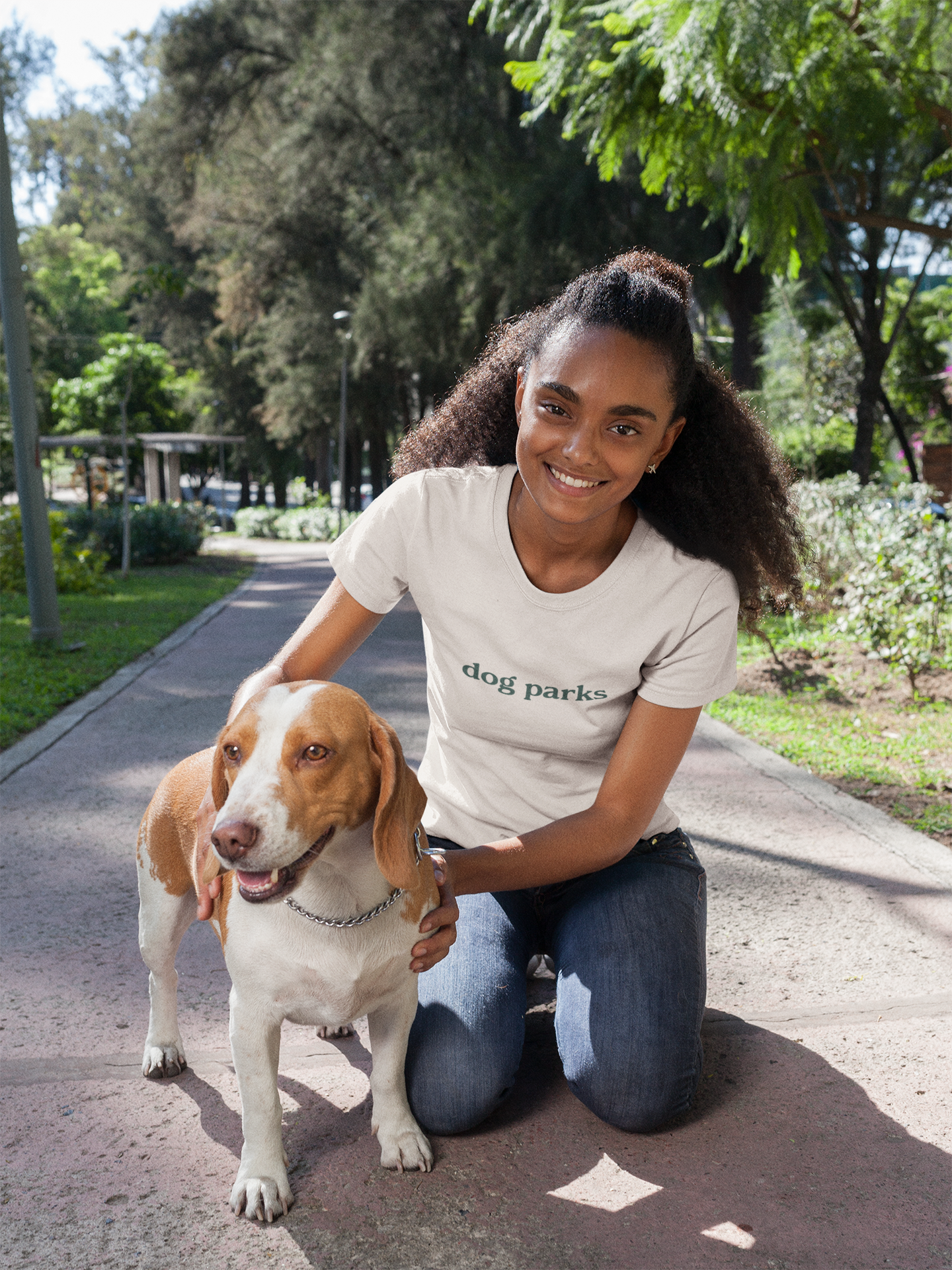 Woman in a 'dog parks' t-shirt sitting on a path with a dog in a park setting