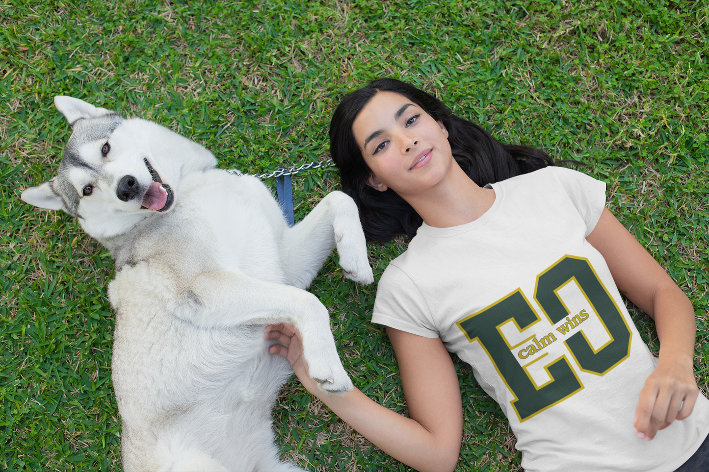 Woman and white dog lying on grass wearing 'Calvin Klein' t-shirt