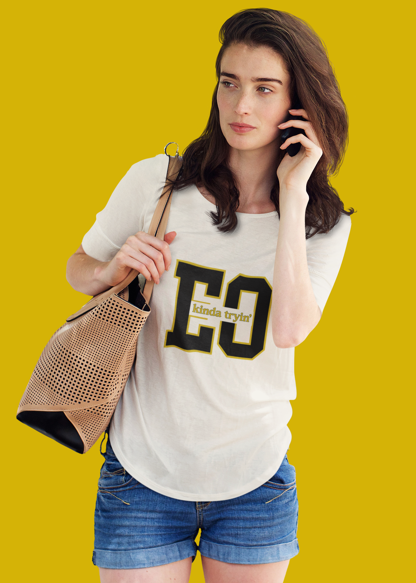 Woman wearing a white t-shirt with 'EC' logo, holding a phone and a handbag against a yellow background