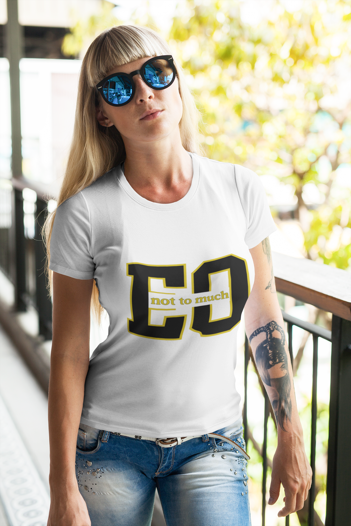 Woman wearing a white t-shirt with 'EC not to much' design, sunglasses, and blue jeans outdoors.