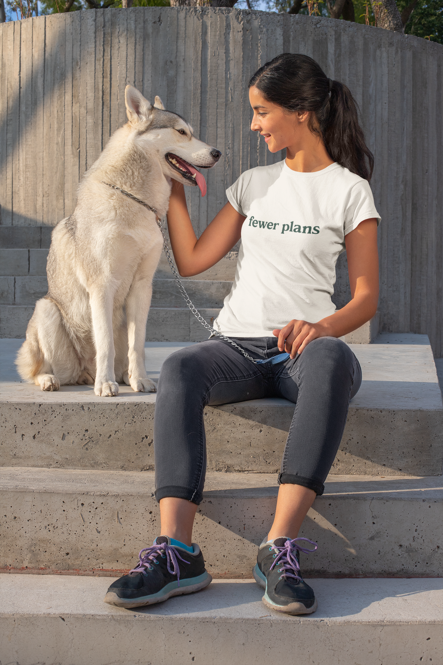 Woman sitting on steps with a dog, wearing a white t-shirt with text, in an outdoor setting.