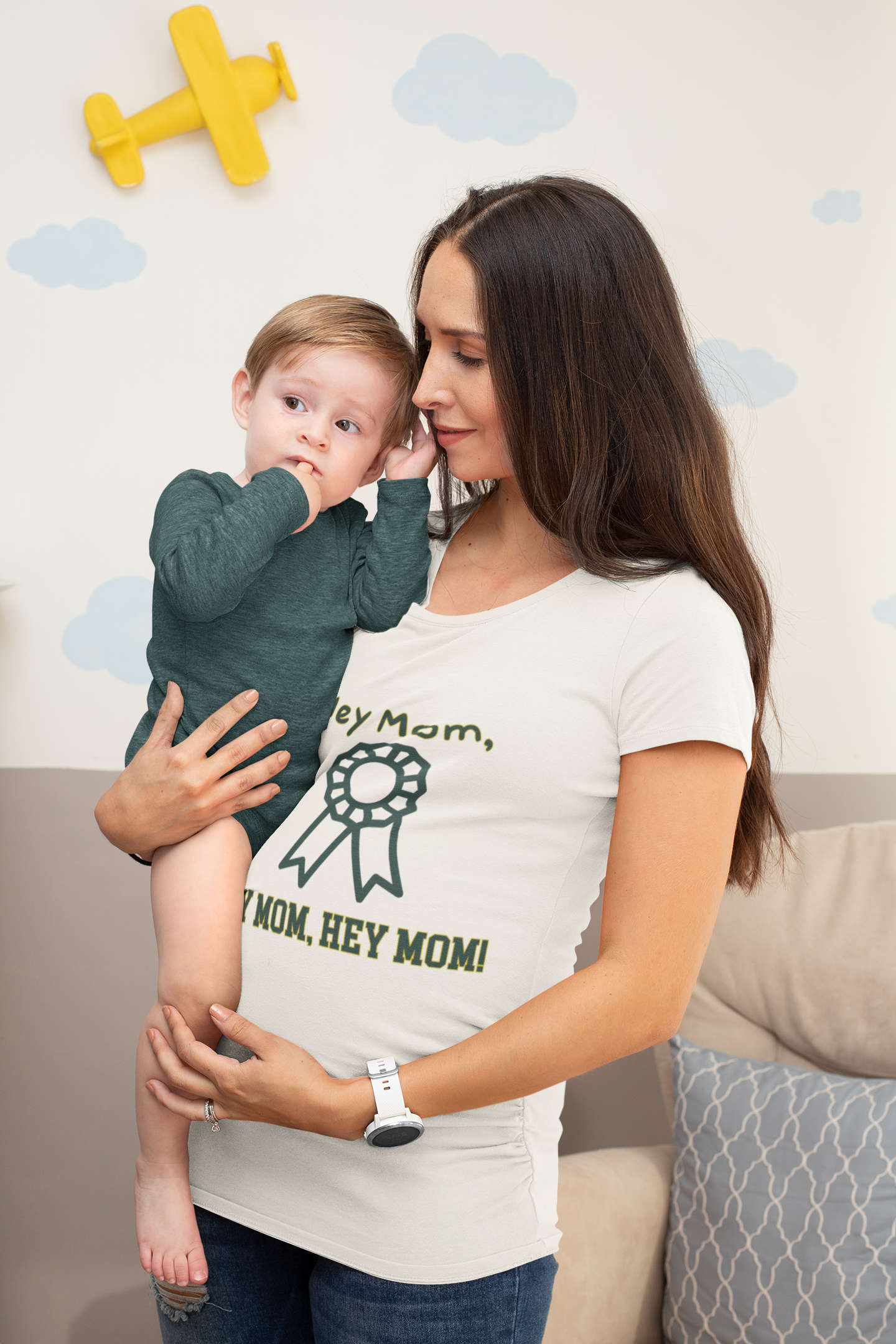 Woman holding a child wearing a shirt with text, sitting on a couch with a decorative wall in the background.