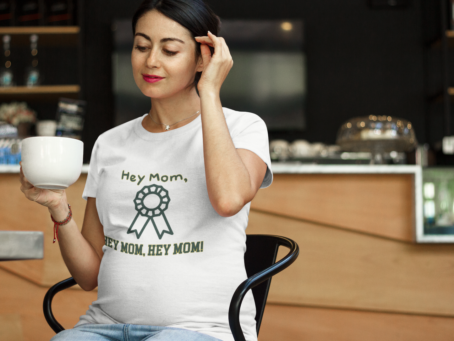 Woman wearing a white t-shirt with 'Hey Mom' text in a coffee shop.