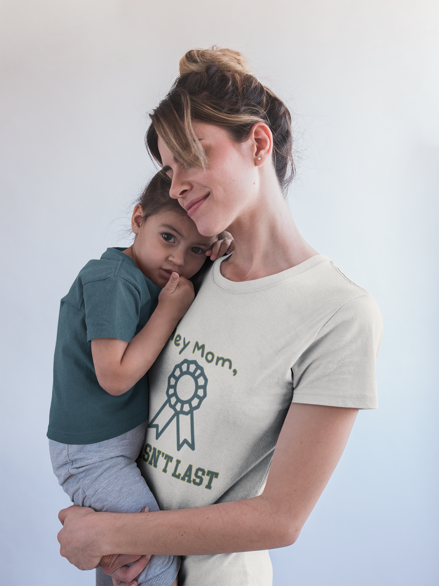 Woman holding a child wearing a t-shirt with text against a plain background