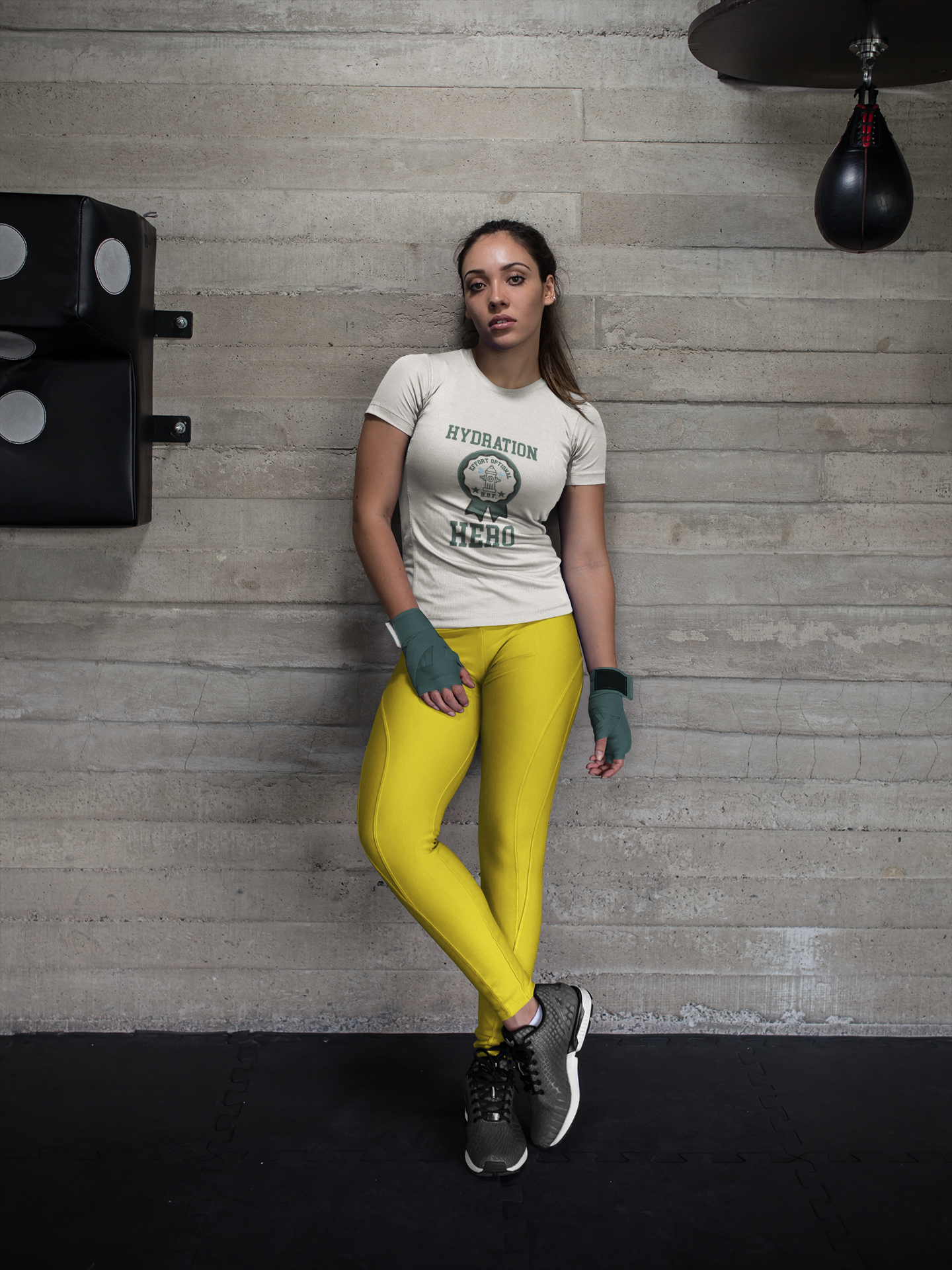 Woman in a gym wearing a t-shirt with text and yellow leggings against a concrete wall.