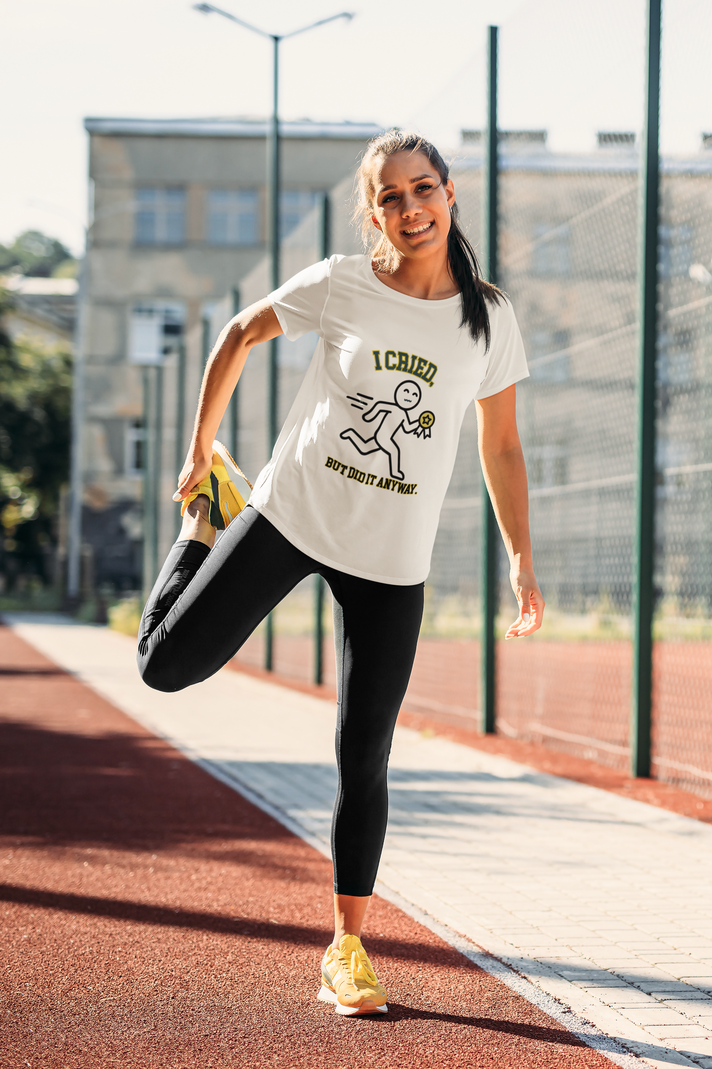 Woman stretching on a running track wearing a white t-shirt with text and graphics.