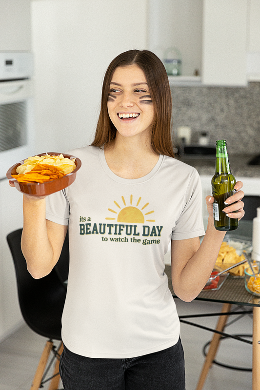 Woman in a kitchen holding chips and a beer, wearing a 'It's a Beautiful Day to Watch the Game' t-shirt.