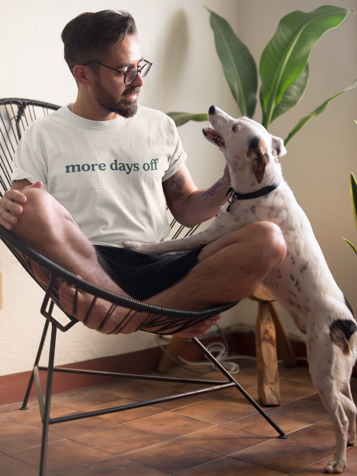 Man sitting on a chair with a dog, wearing a 'more days off' t-shirt.