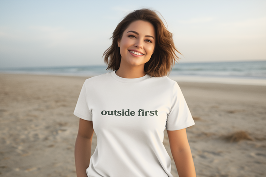 Woman wearing a white t-shirt with 'outside first' text on a beach