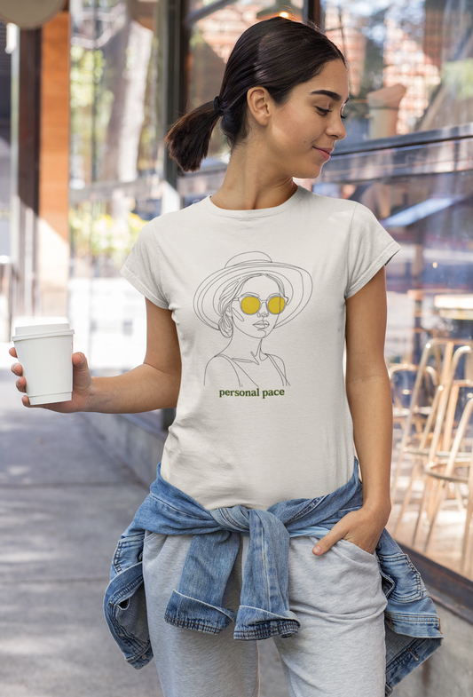 Woman wearing a t-shirt with a graphic design and text, holding a cup outdoors.