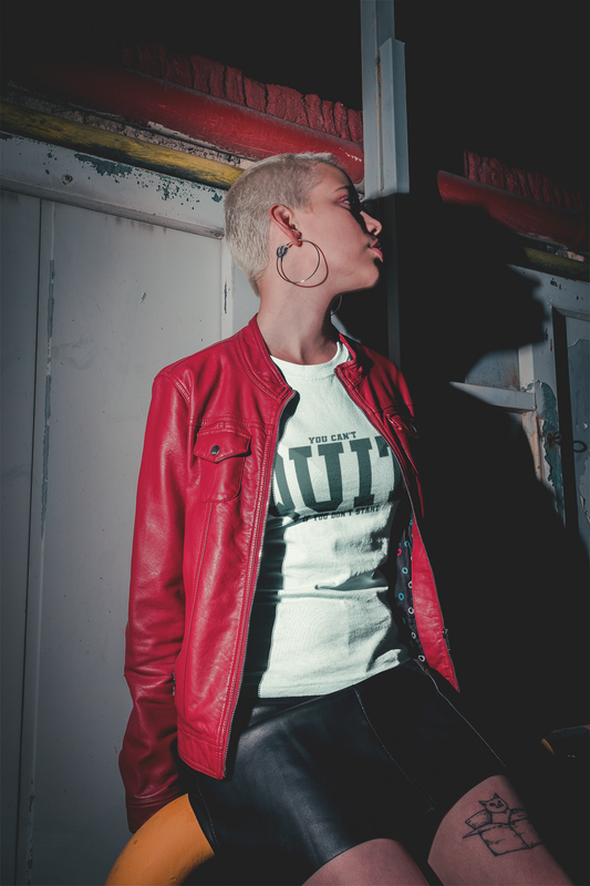 Person wearing a red jacket and black leather pants with a white graphic t-shirt, standing against a dark background.