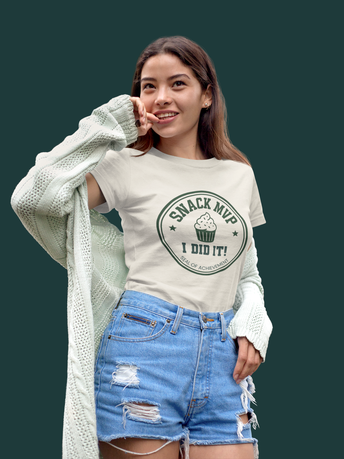Woman wearing a t-shirt with 'Snack MVP I Did It!' text and graphics, standing against a dark green background.
