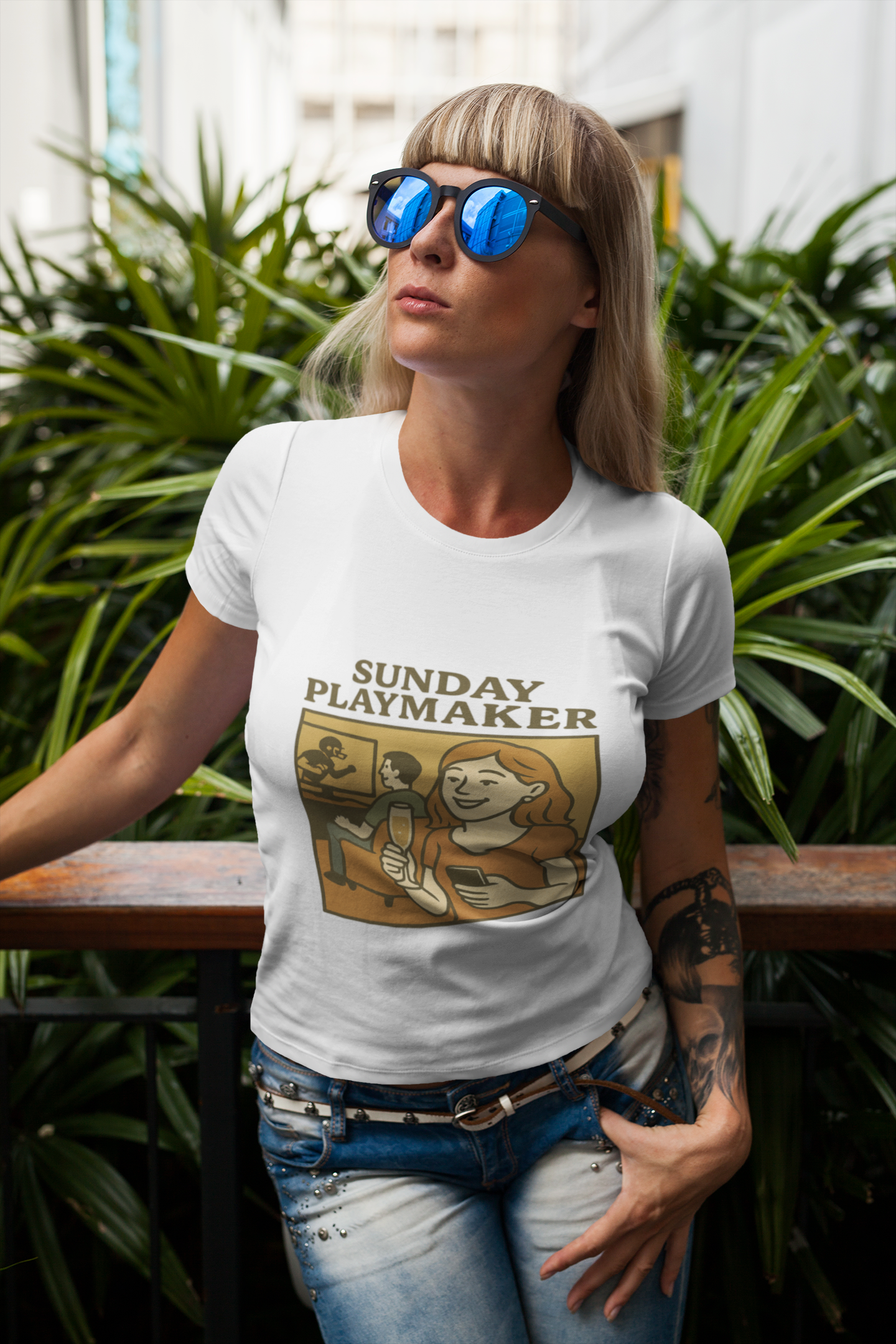 Woman wearing a white t-shirt with 'Sunday Playmaker' graphic design, standing outdoors with plants in the background.