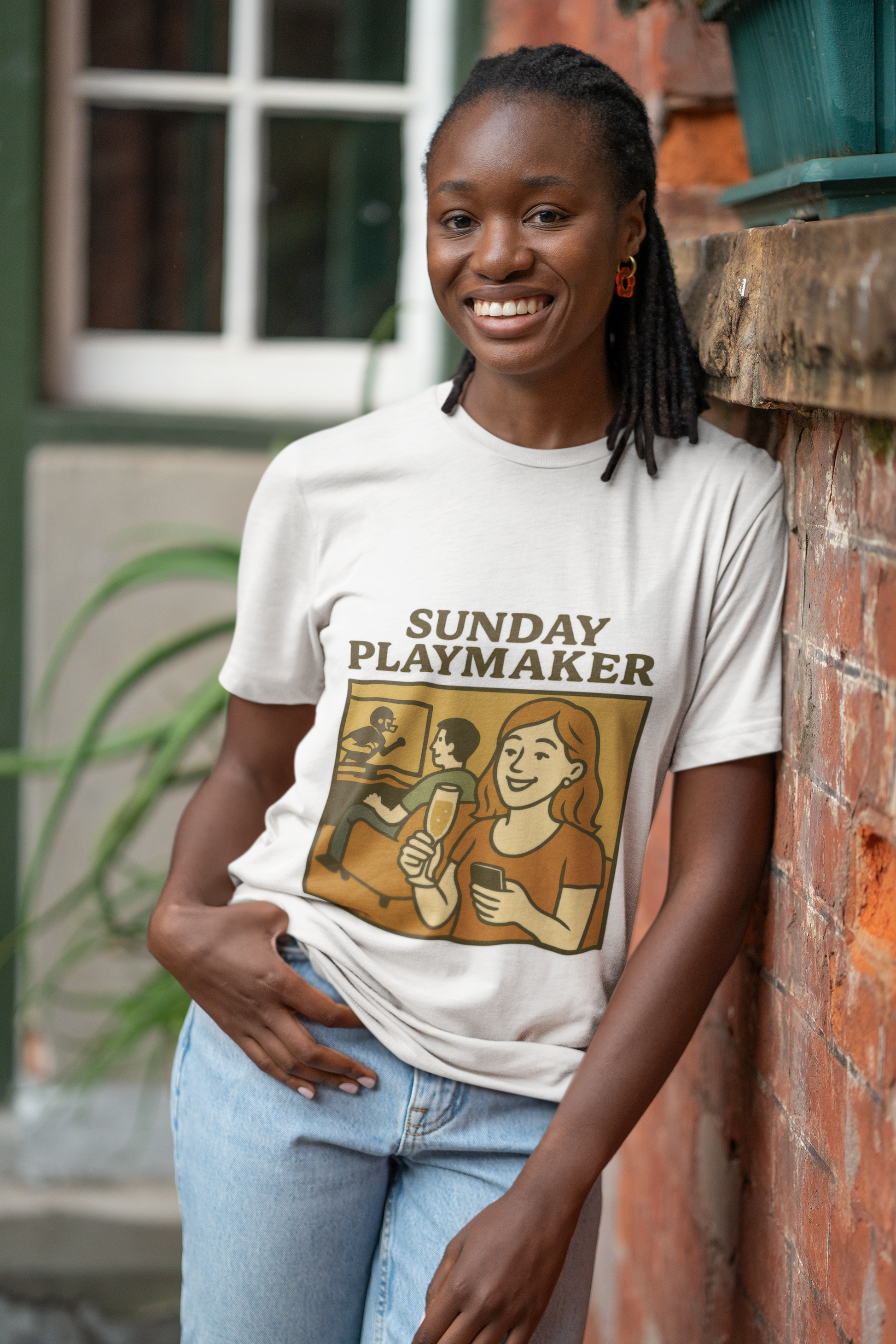 Woman wearing a 'Sunday Playmaker' t-shirt leaning against a brick wall.