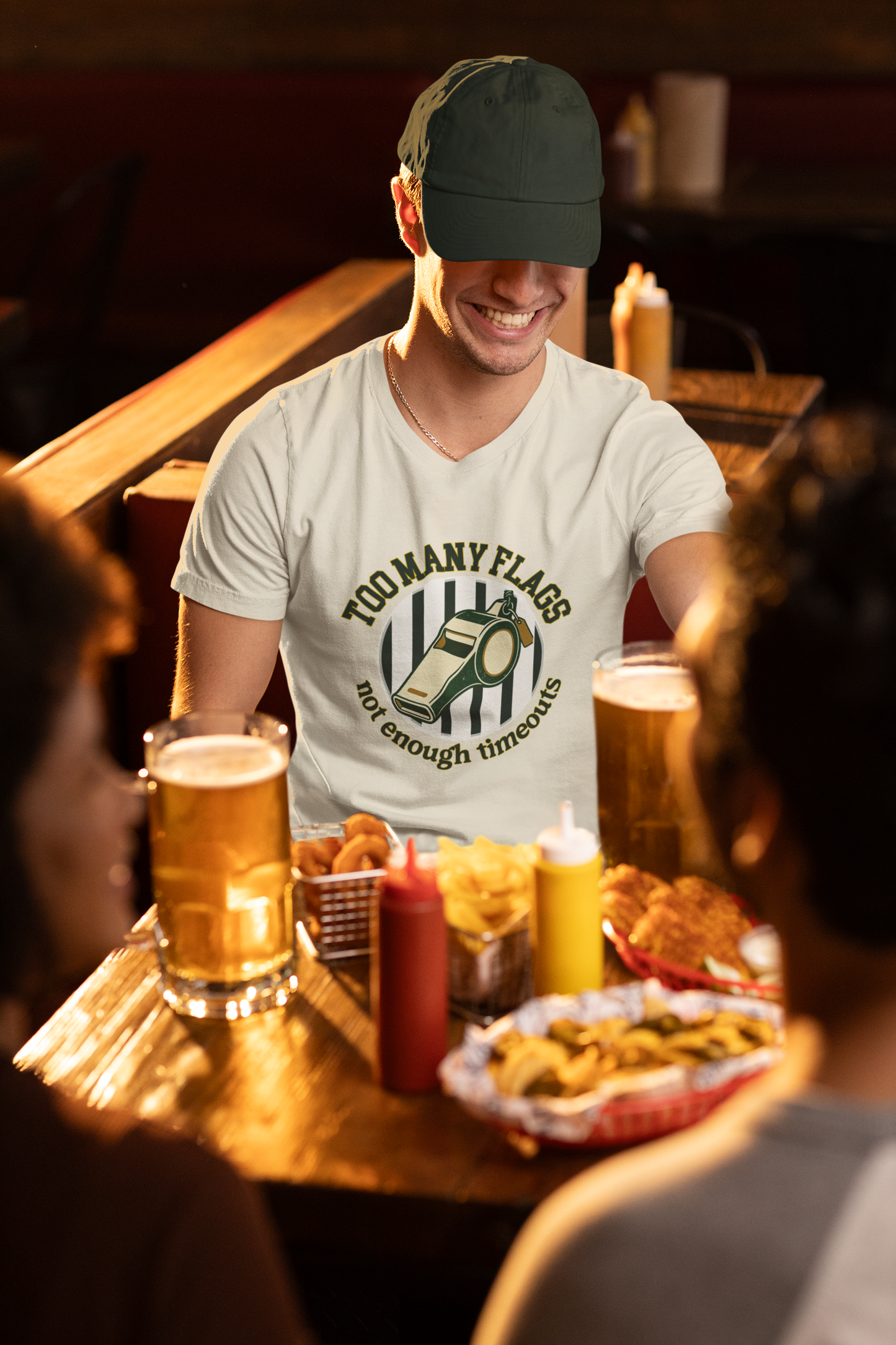 Man sitting at a bar with drinks and snacks, wearing a white t-shirt with a graphic design.