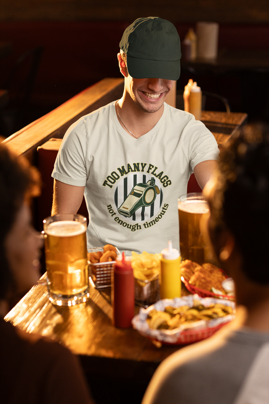 Man sitting at a bar with drinks and snacks, wearing a white t-shirt with a graphic design.