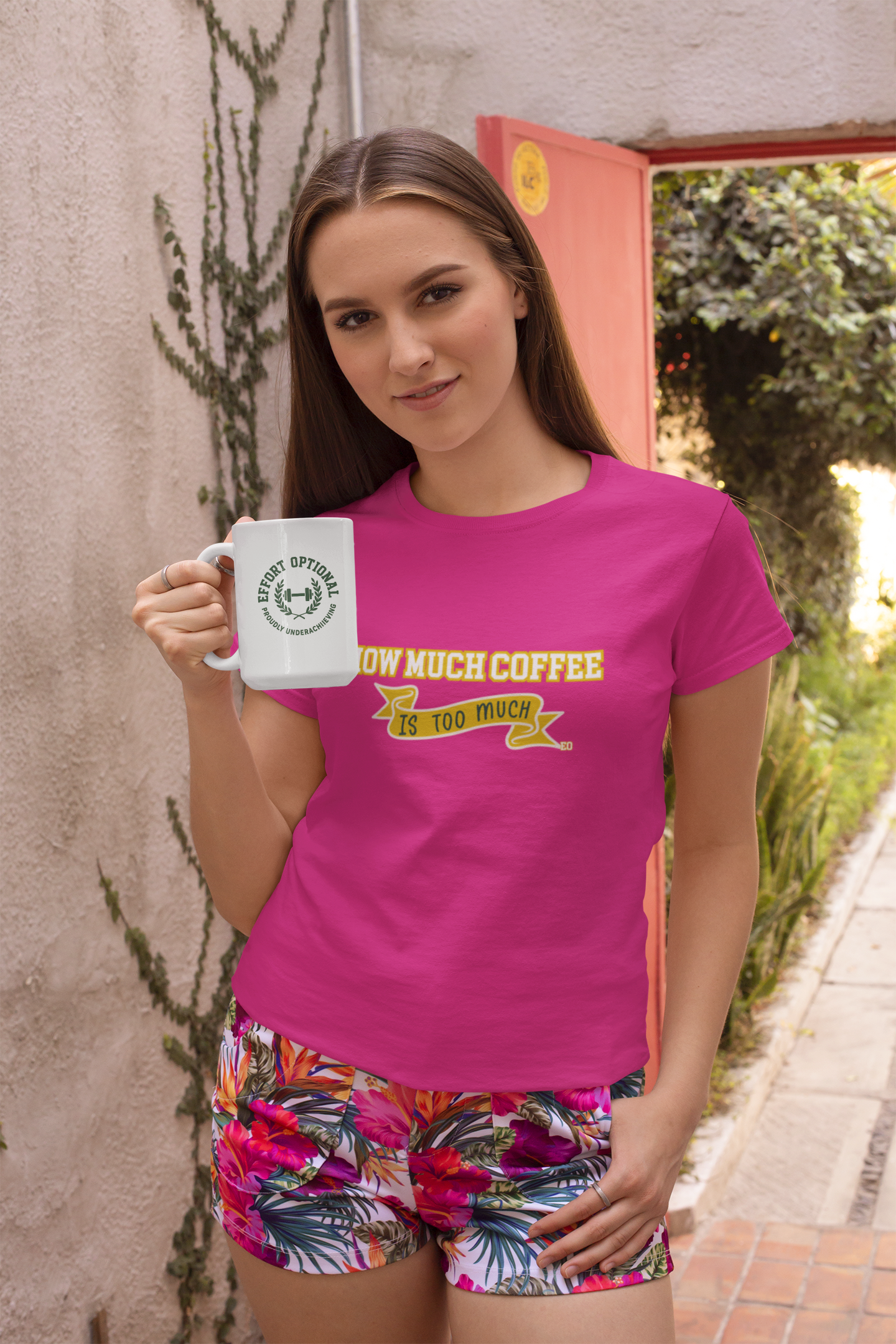 Woman wearing a pink t-shirt with text and colorful shorts, holding a coffee mug.