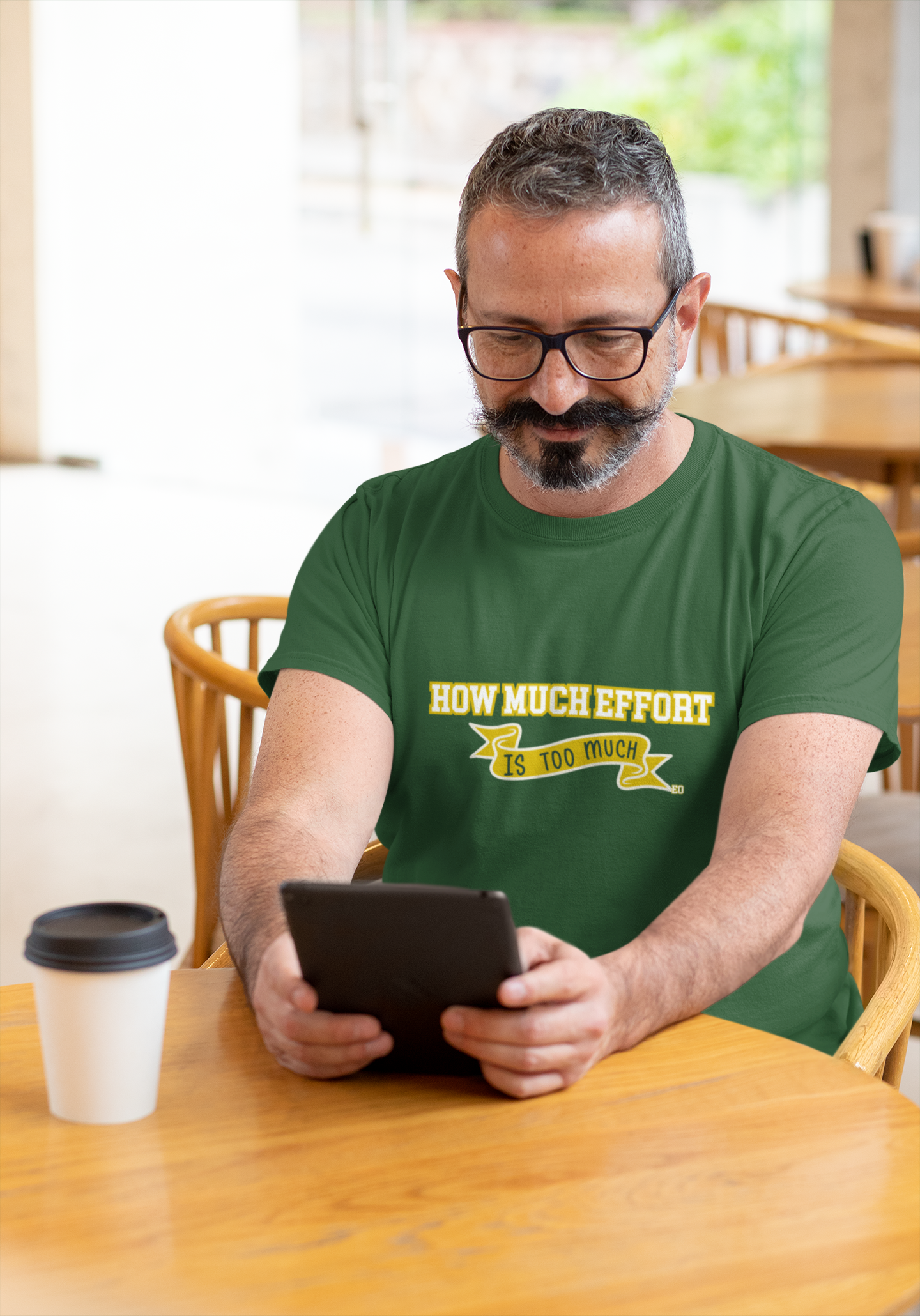 Man wearing a green t-shirt with text, using a tablet at a table.