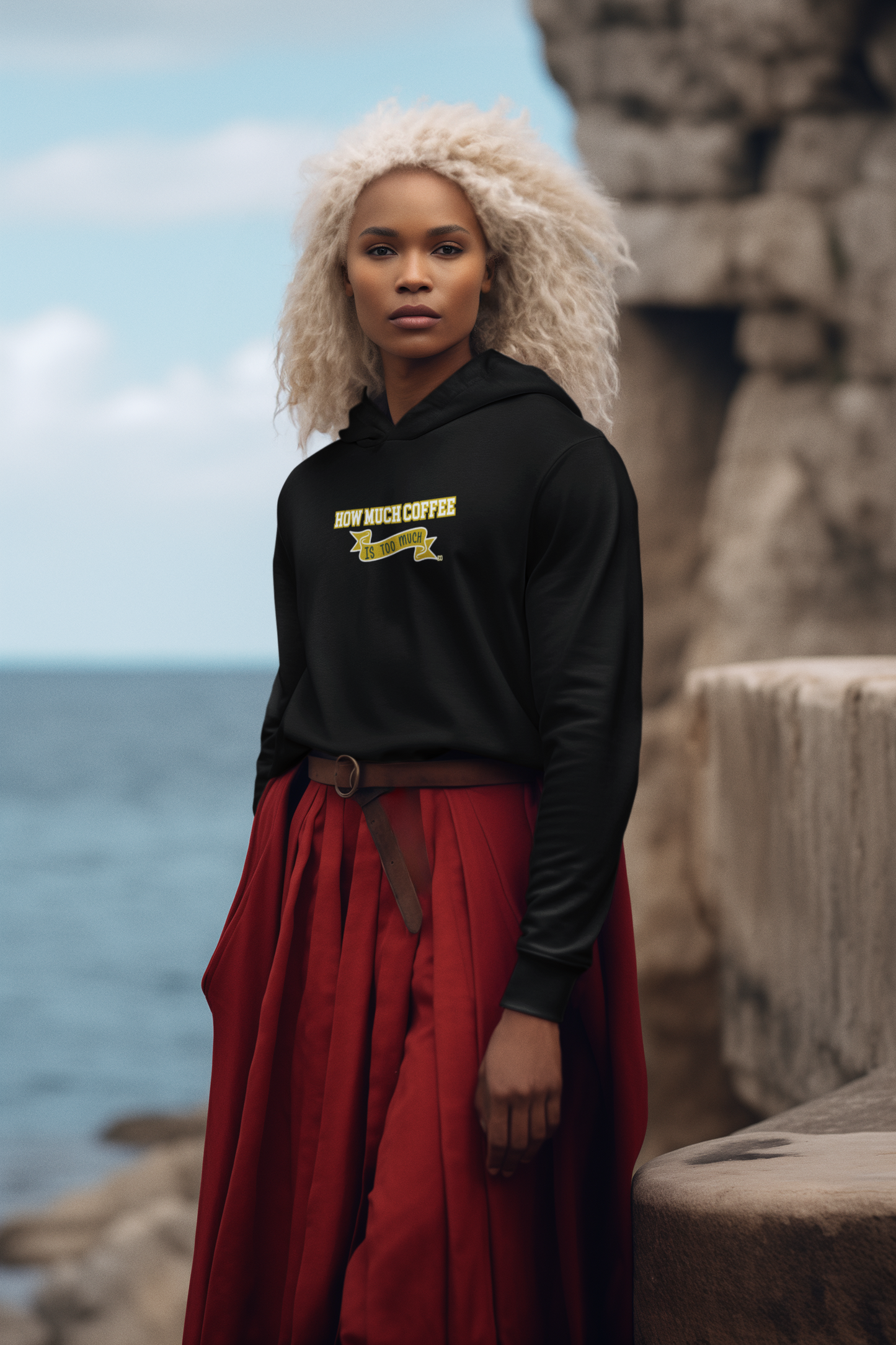 Person wearing a black hoodie with yellow text and red pants standing by the ocean.