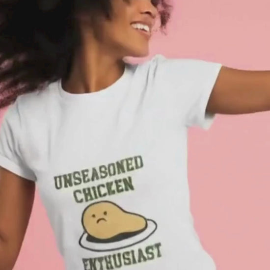 Woman wearing a t-shirt with 'Unseasoned Chicken Enthusiast' graphic on a pink background.video