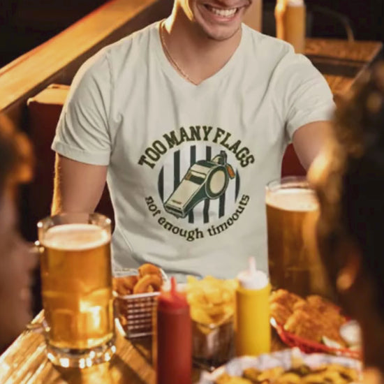 Man sitting at a bar with drinks and snacks, wearing a white t-shirt with a graphic design..video