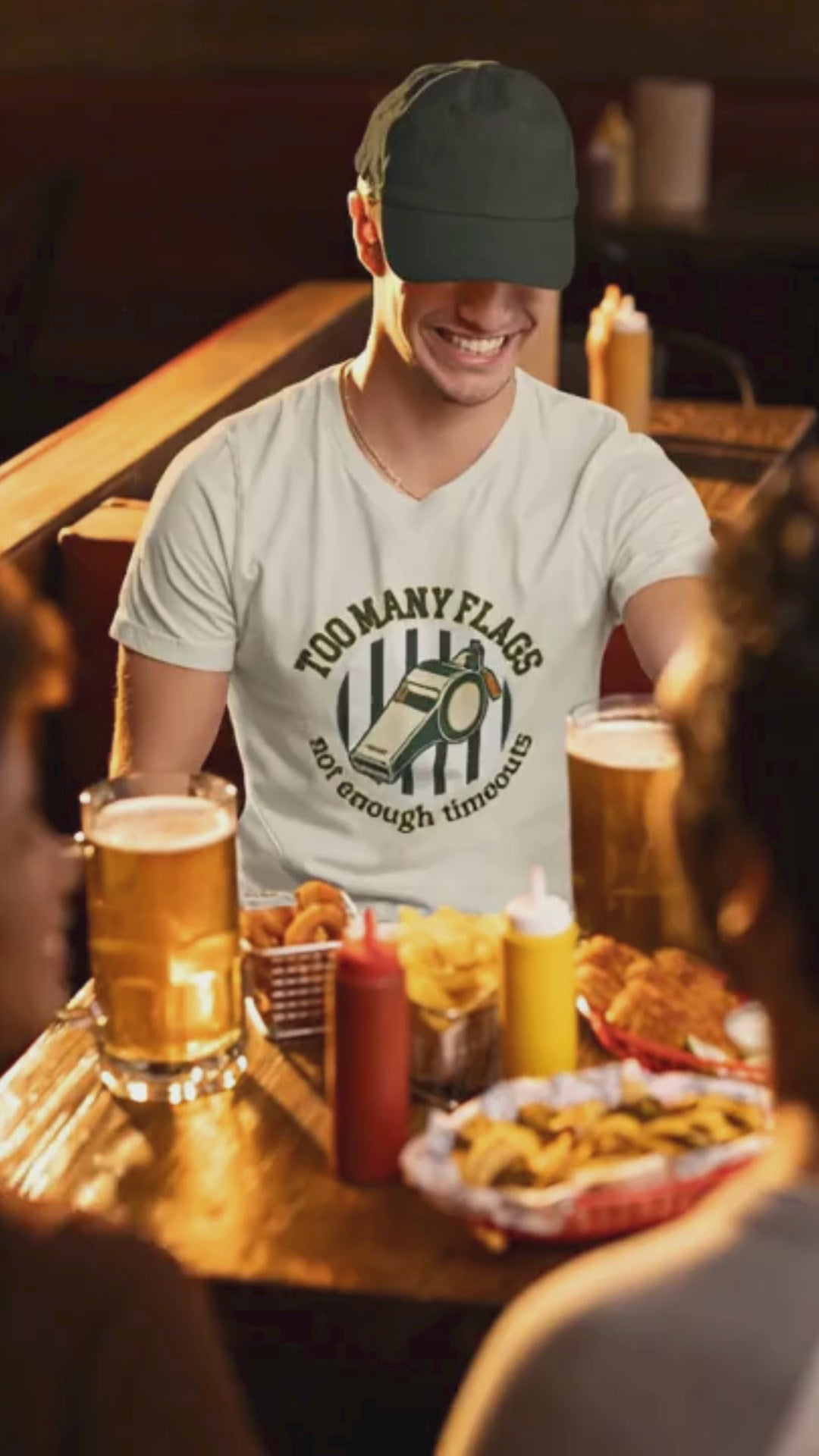 Man sitting at a bar with drinks and snacks, wearing a white t-shirt with a graphic design..video