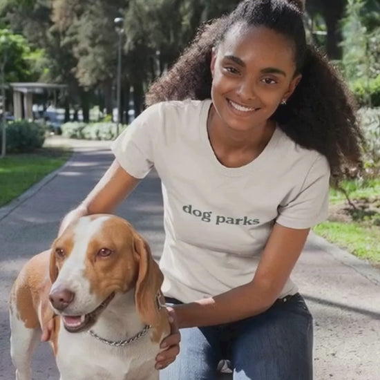 Woman in a 'dog parks' t-shirt sitting on a path with a dog in a park setting.video