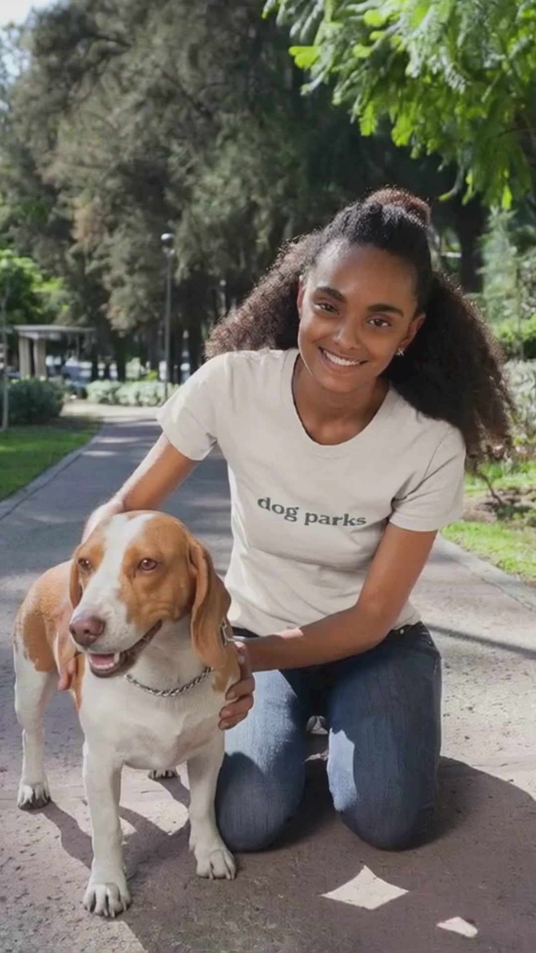 Woman in a 'dog parks' t-shirt sitting on a path with a dog in a park setting.video
